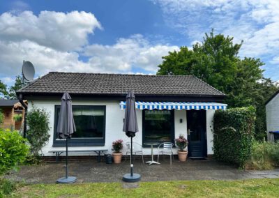 Ferienhaus am Wittensee - vom Garten aus fotografiert - Blick auf die Terrasse, 2 Fenster, 1 Tür, Markise, 2 Schirme.